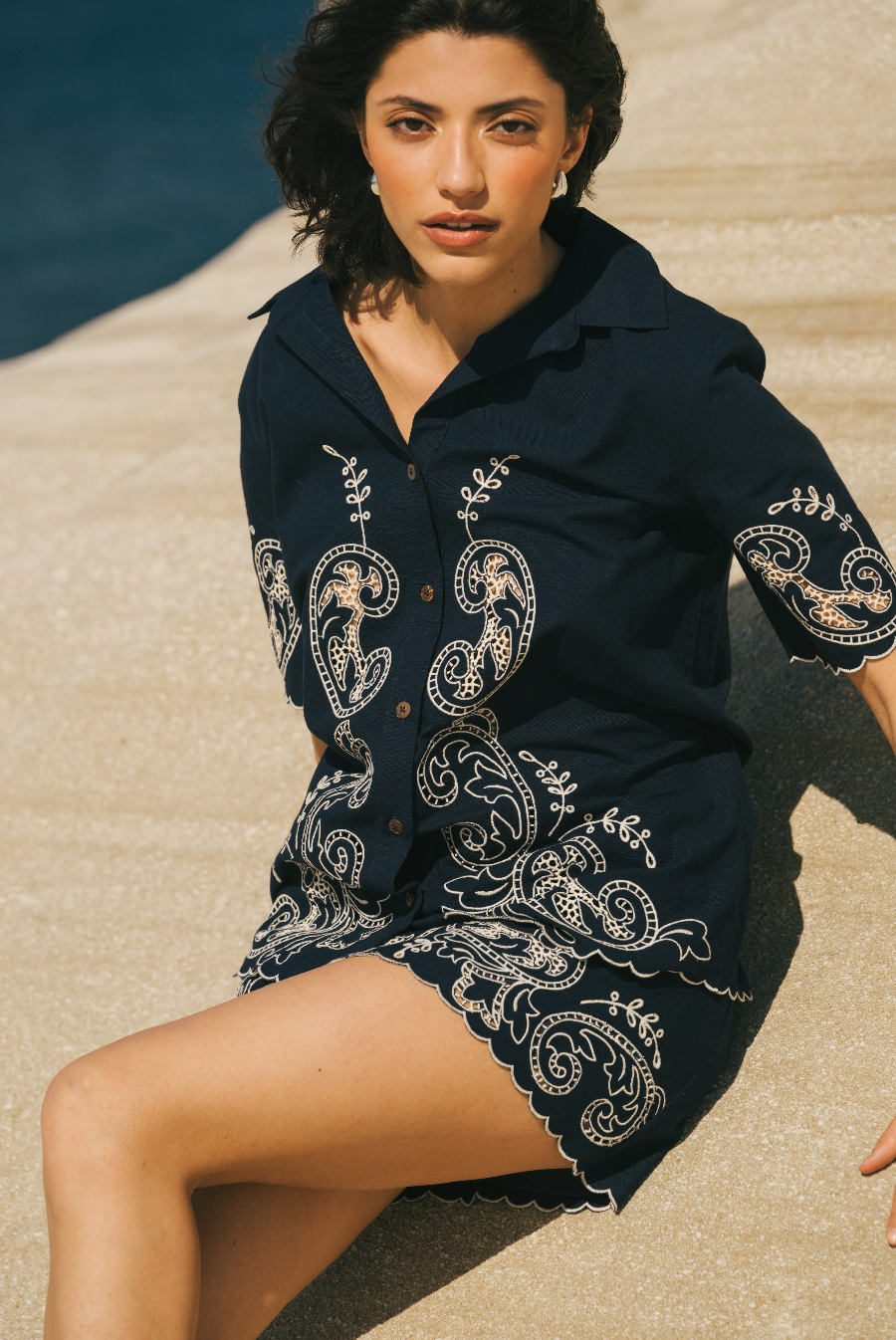 Woman wearing a black embroidered dress sitting by a poolside Calling June