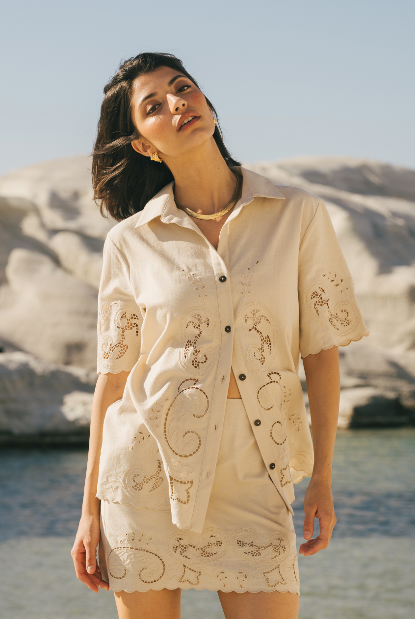 Woman wearing a beige embroidered outfit on a beach with sand dunes in the background Calling June