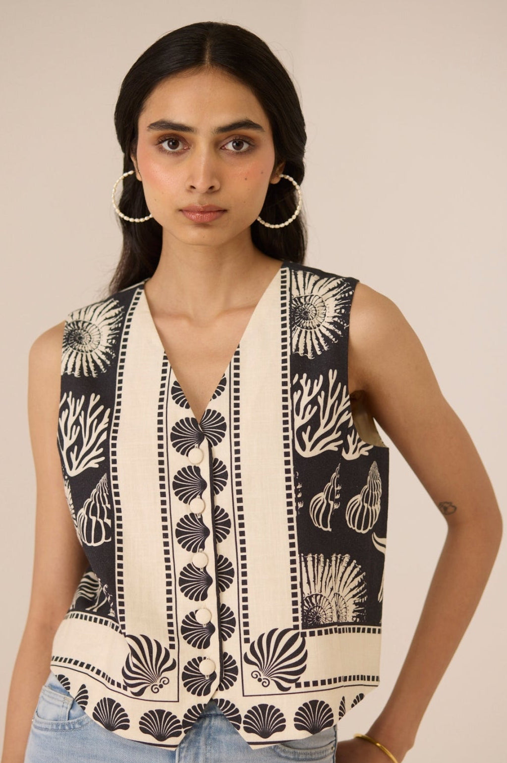 Woman wearing a sleeveless top with a black and white pattern against a beige background Calling June