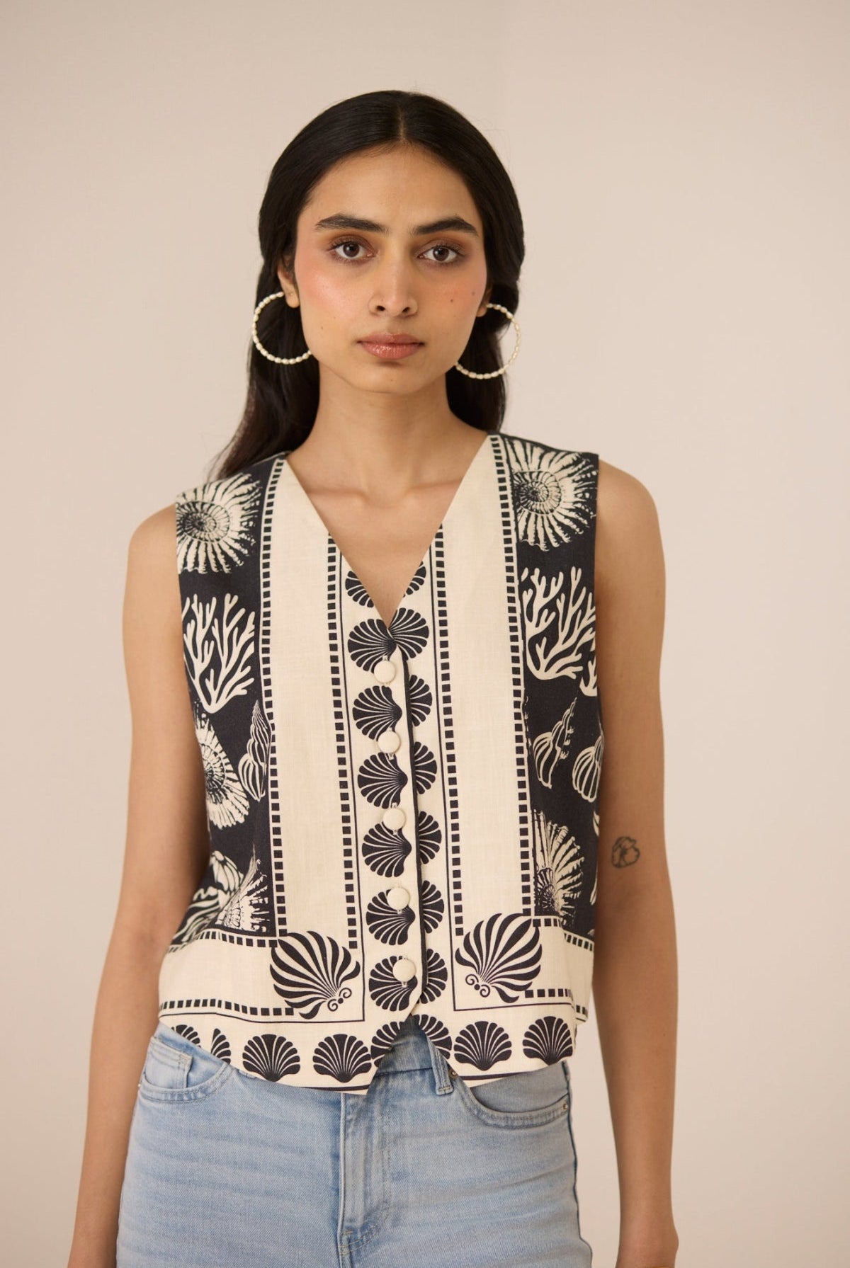 Woman wearing a sleeveless top with black and white pattern against a beige background Calling June