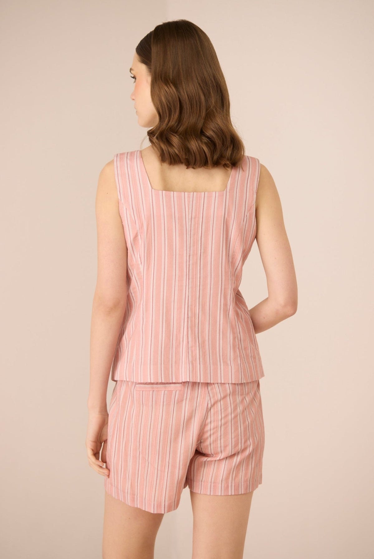 Woman wearing a pink striped sleeveless top and shorts set on a beige background Calling June