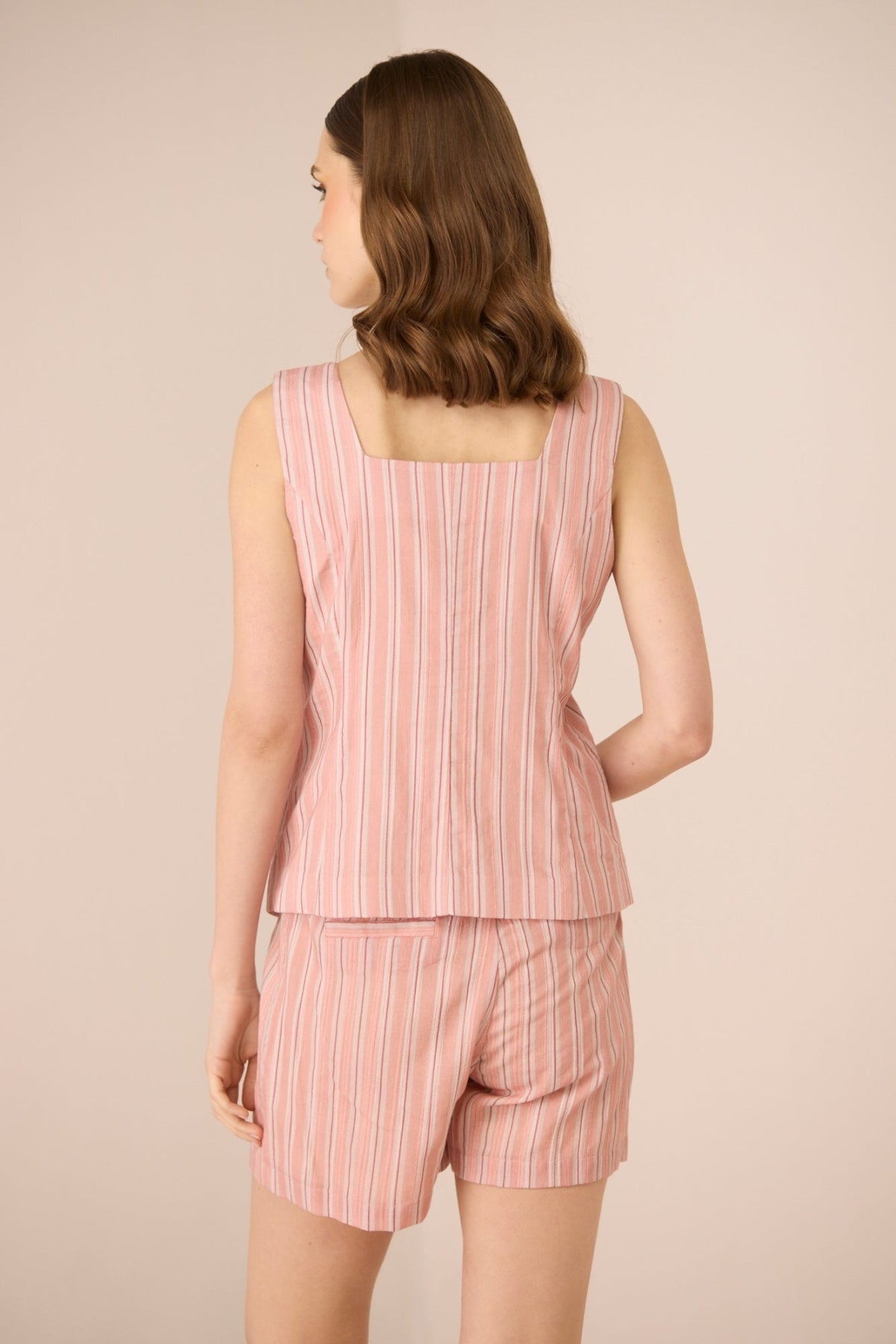 Woman wearing a pink striped sleeveless top and shorts set on a beige background Calling June