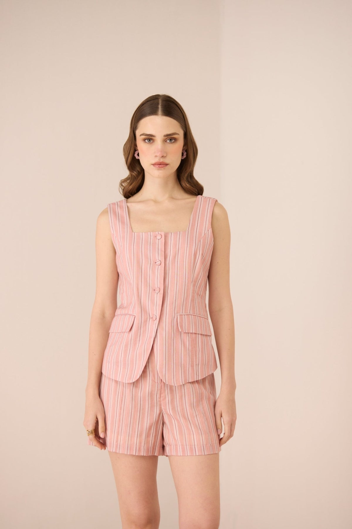 Woman wearing a pink striped outfit with a vest and shorts on a beige background Calling June