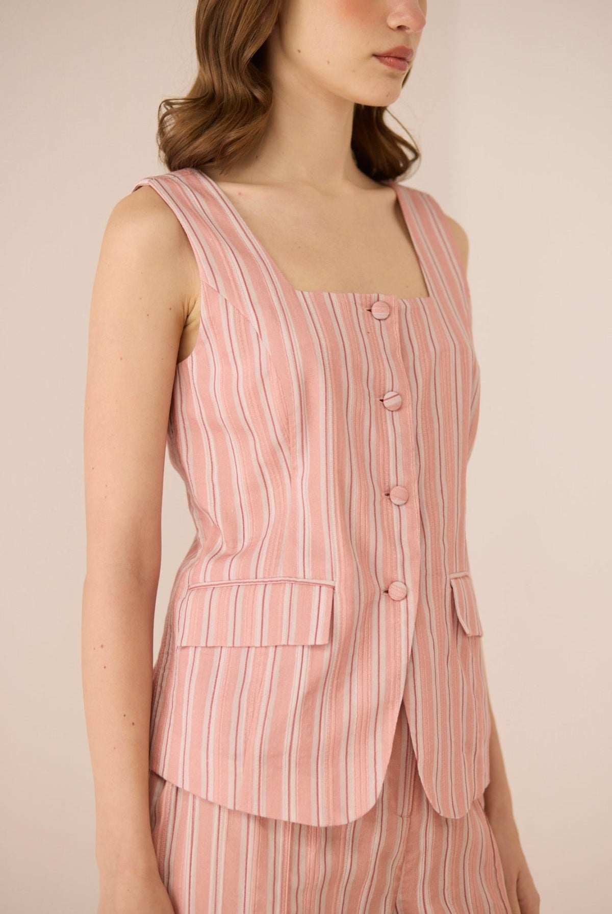 Woman wearing a pink striped sleeveless blazer over a matching dress against a beige background Calling June