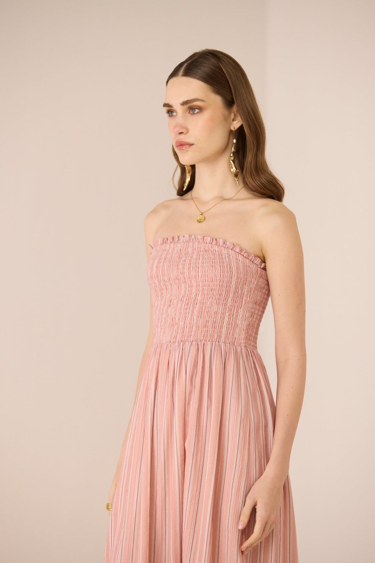 Woman wearing a pink strapless dress against a beige background Calling June