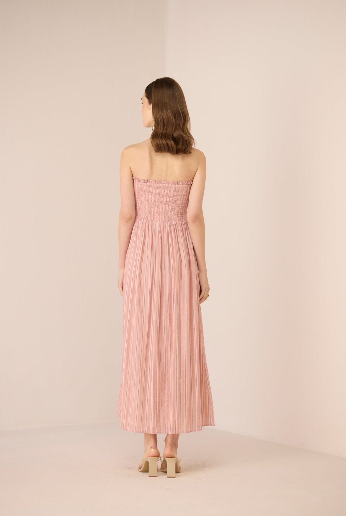 Woman wearing a pink strapless dress against a plain background Calling June