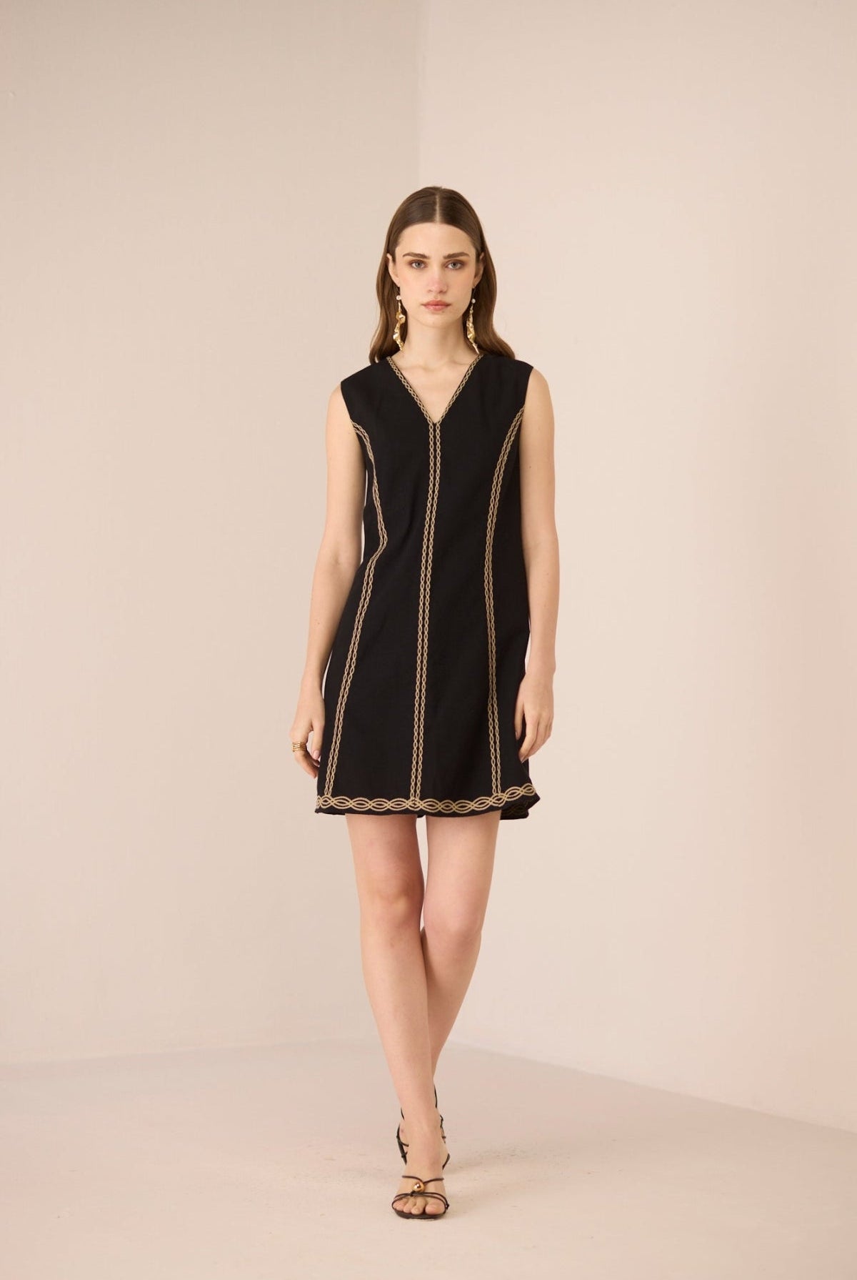 Woman wearing a black dress with gold trim on a beige background Calling June