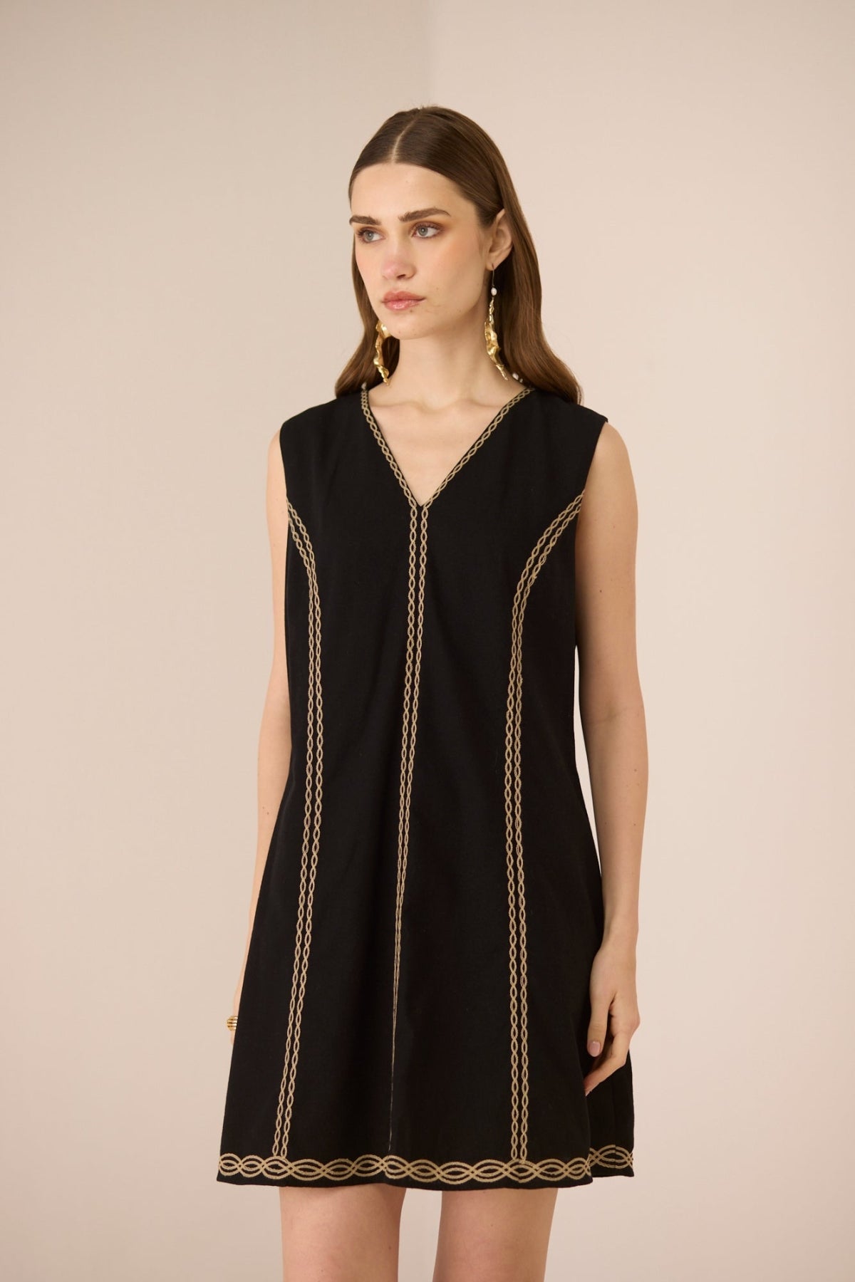 Woman wearing a black sleeveless dress with gold trim on a beige background Calling June