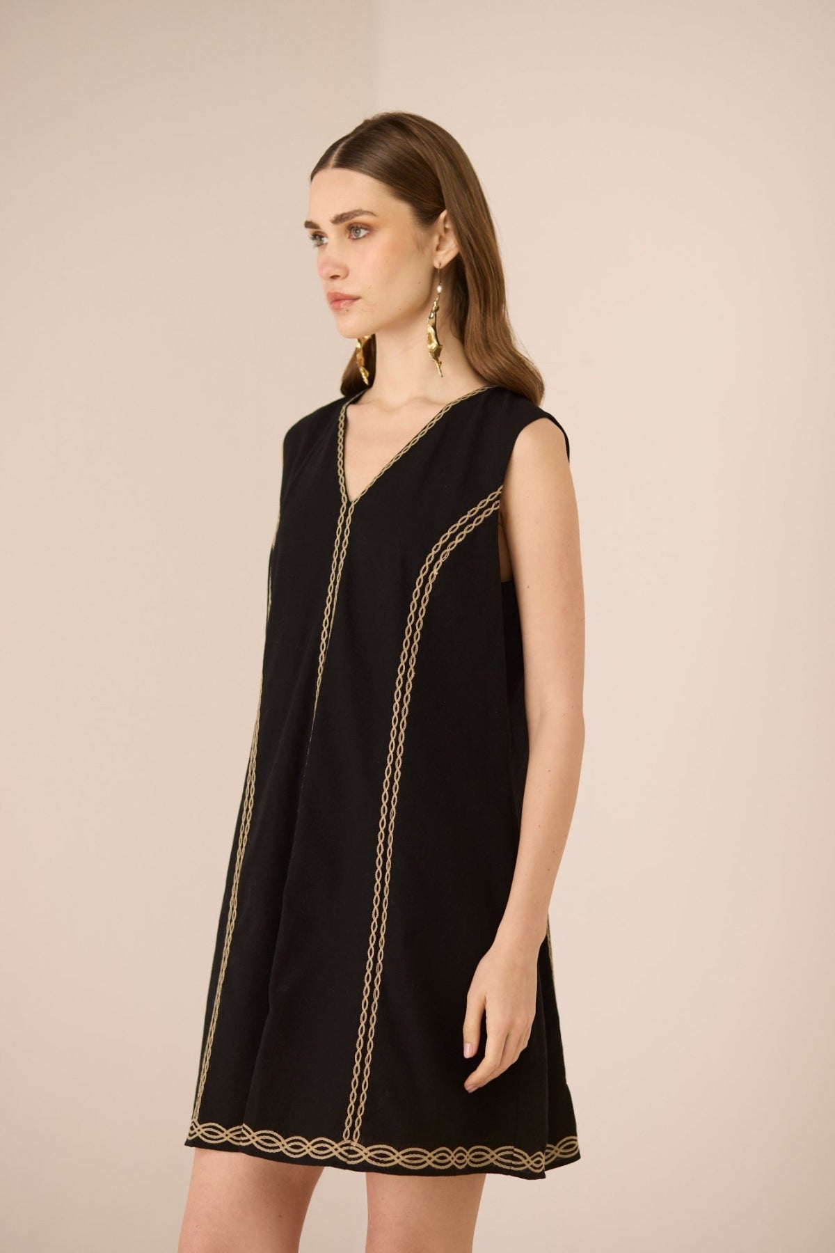 Woman wearing a black dress with gold trim on a beige background Calling June