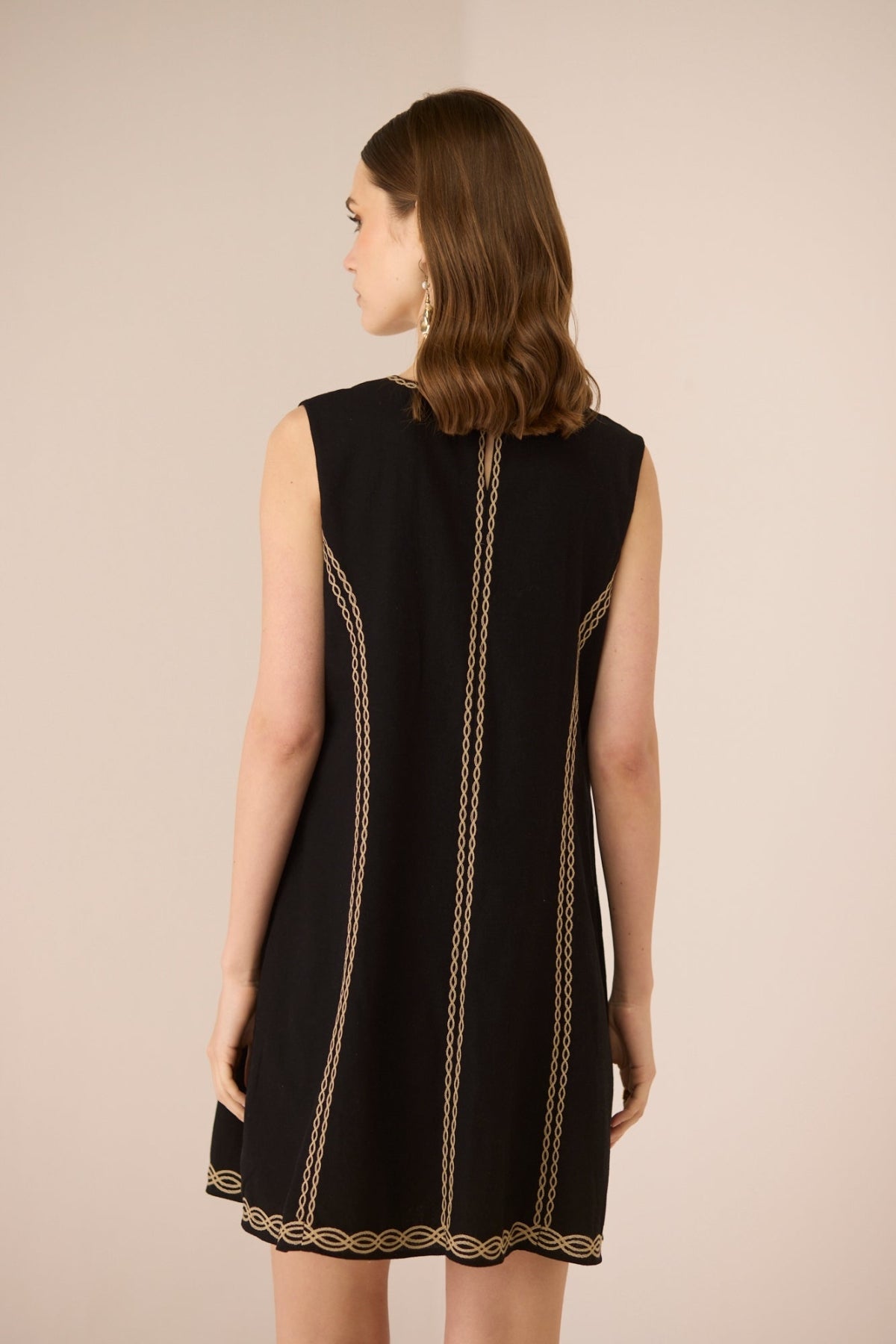 Black sleeveless dress with gold trim on a beige background Calling June