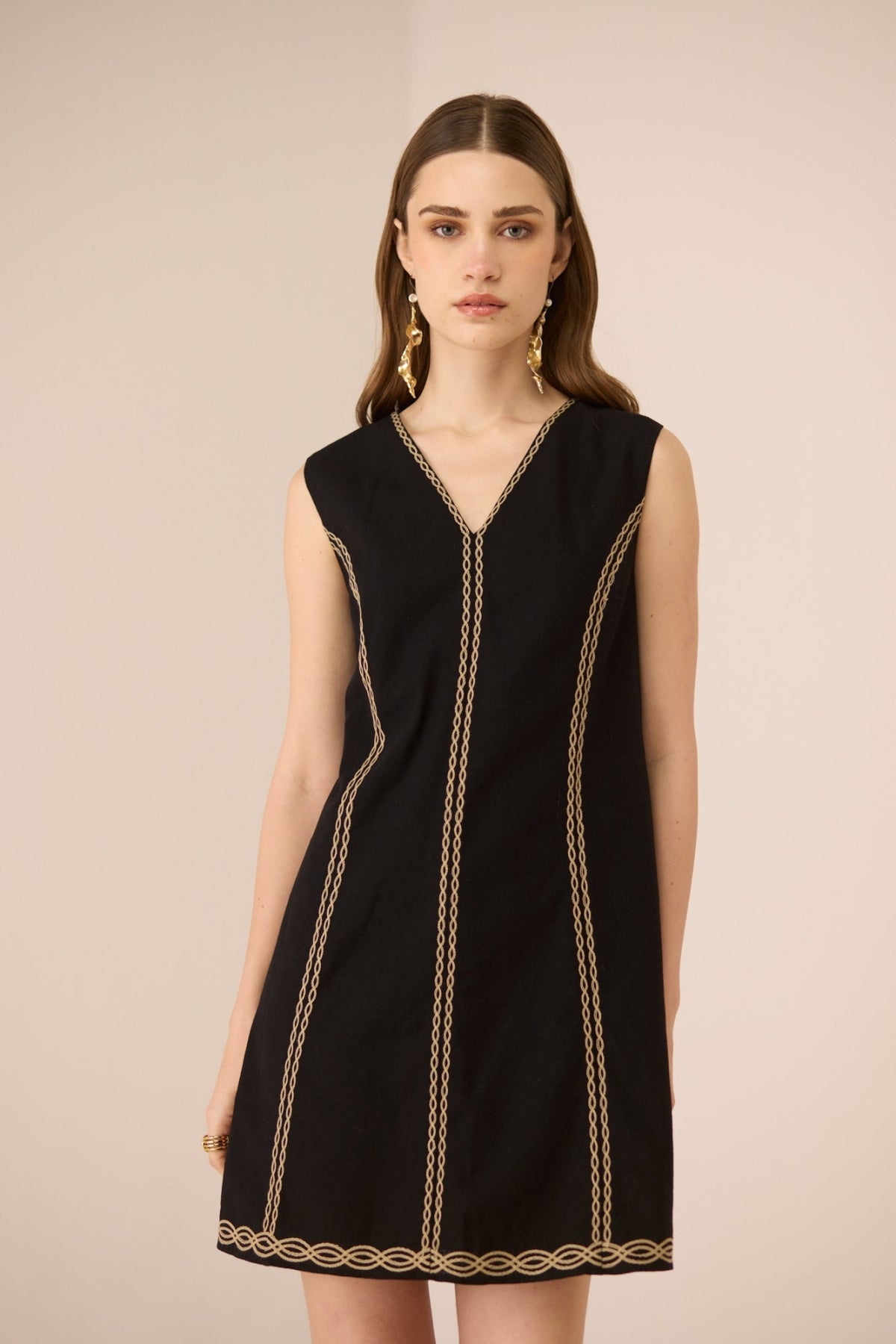 Black dress with gold trim worn by a model on a beige background Calling June
