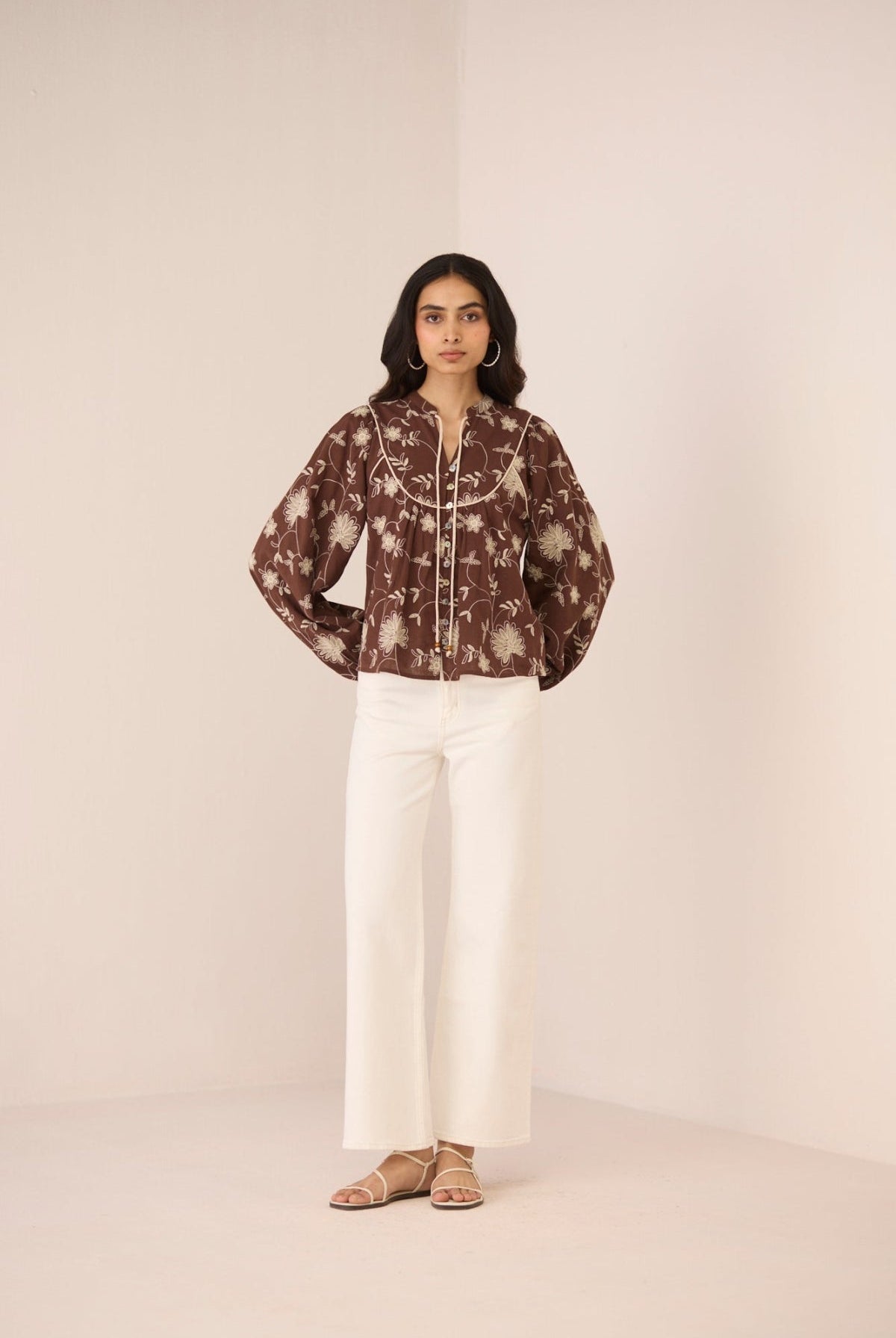 Woman wearing a patterned blouse and white pants against a plain background Calling June