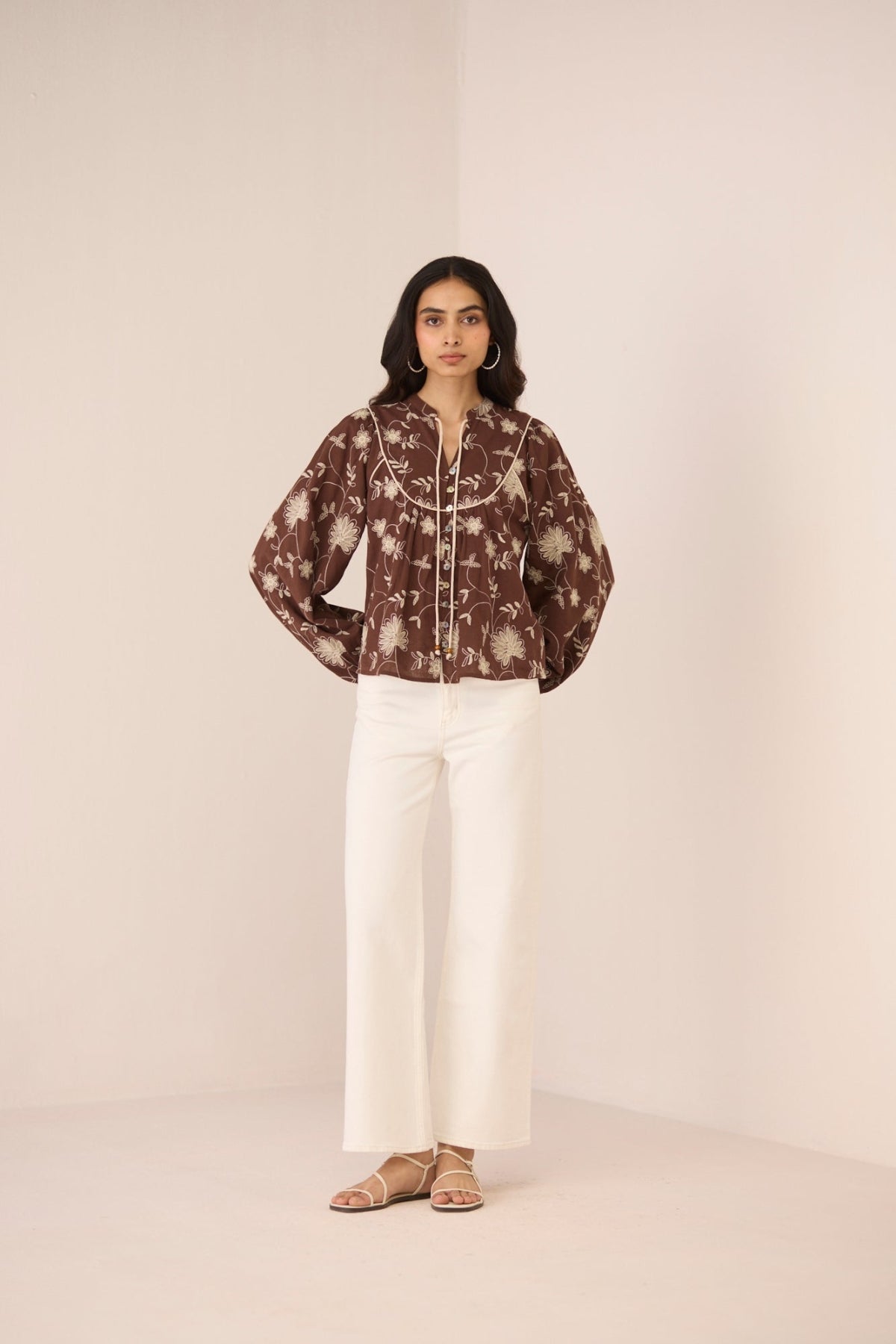 Woman wearing a patterned blouse and white pants against a plain background Calling June