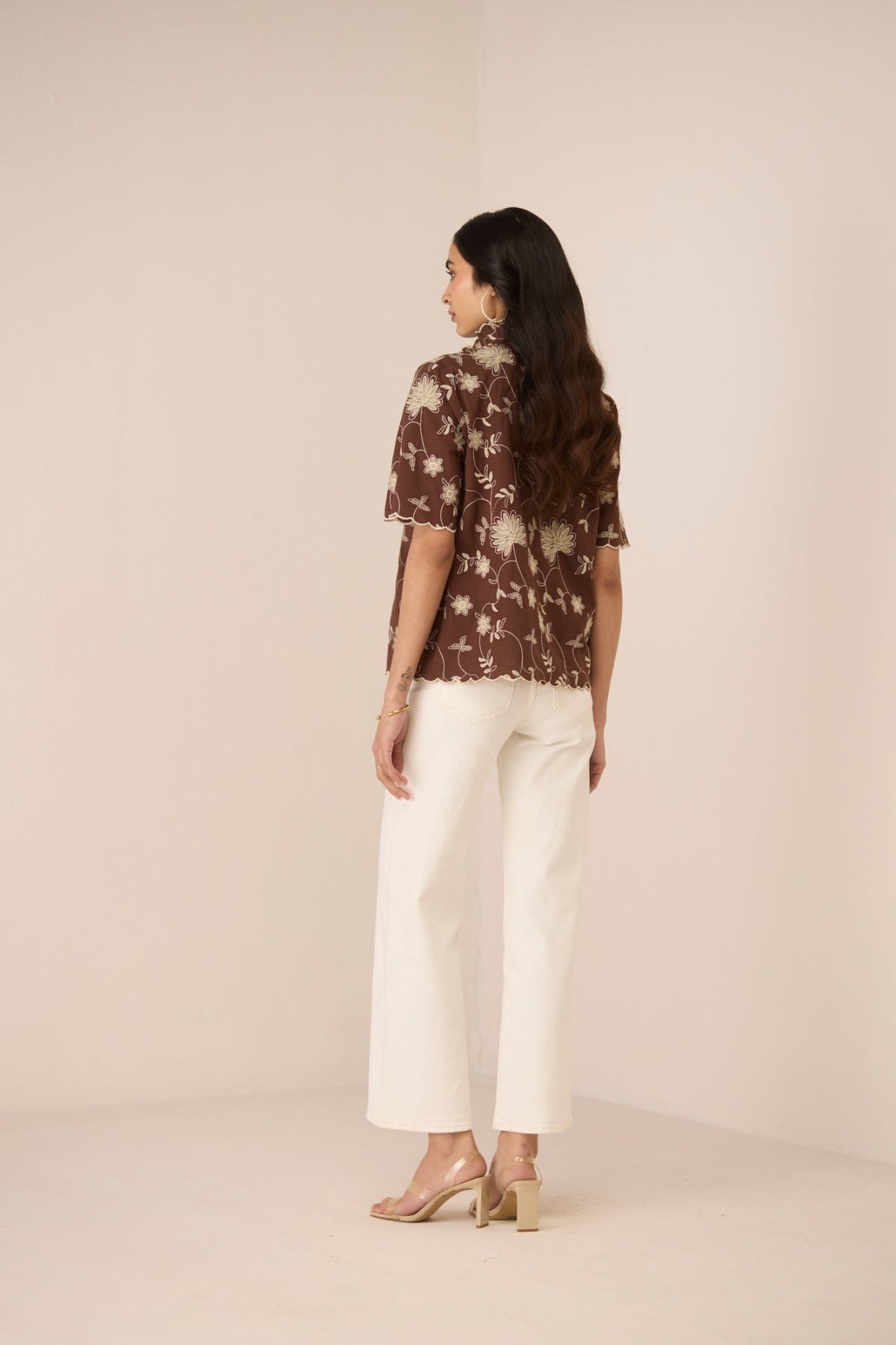 Woman wearing a brown floral blouse and white pants on a beige background Calling June