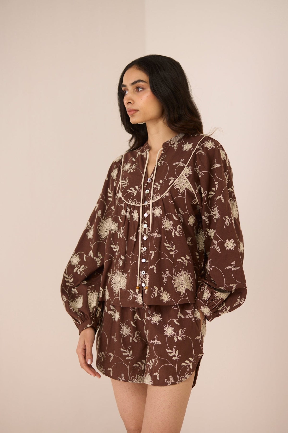 Woman wearing a brown floral patterned outfit against a plain background Calling June