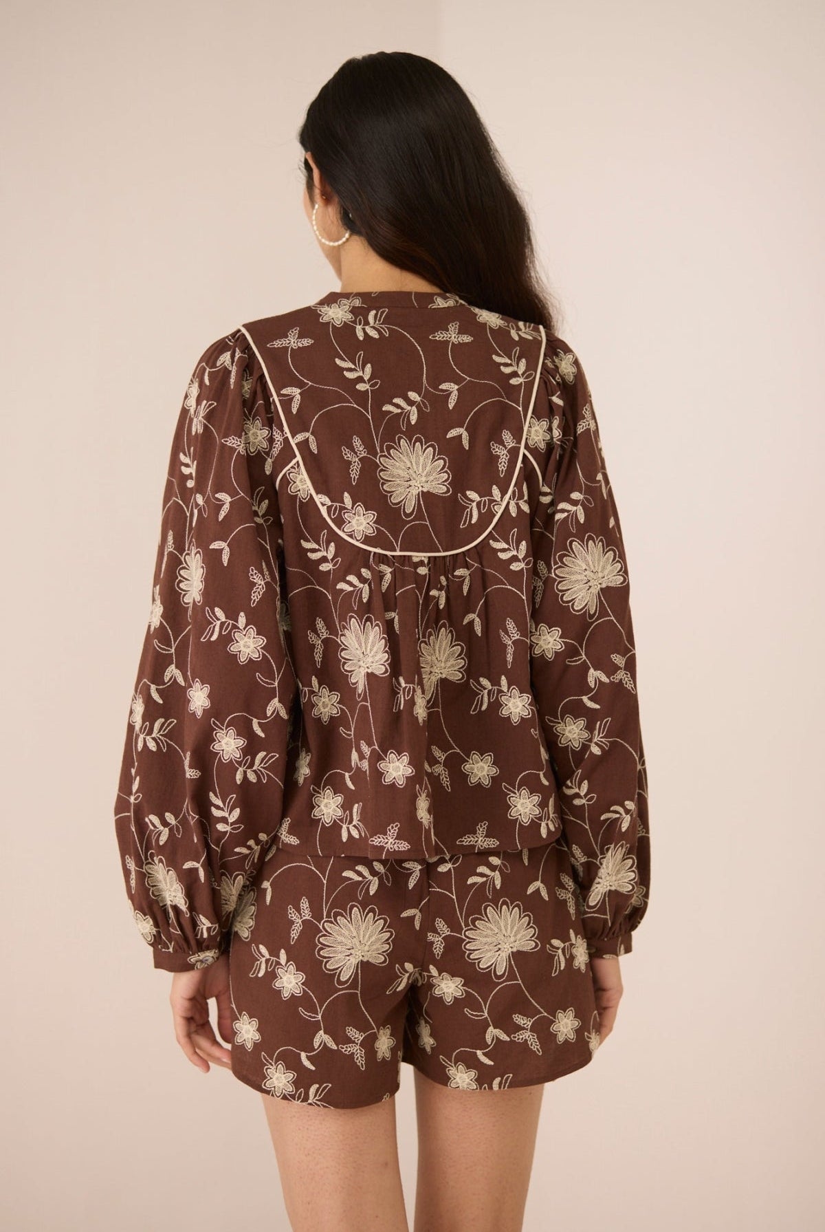 Woman wearing a brown floral patterned outfit against a plain background Calling June