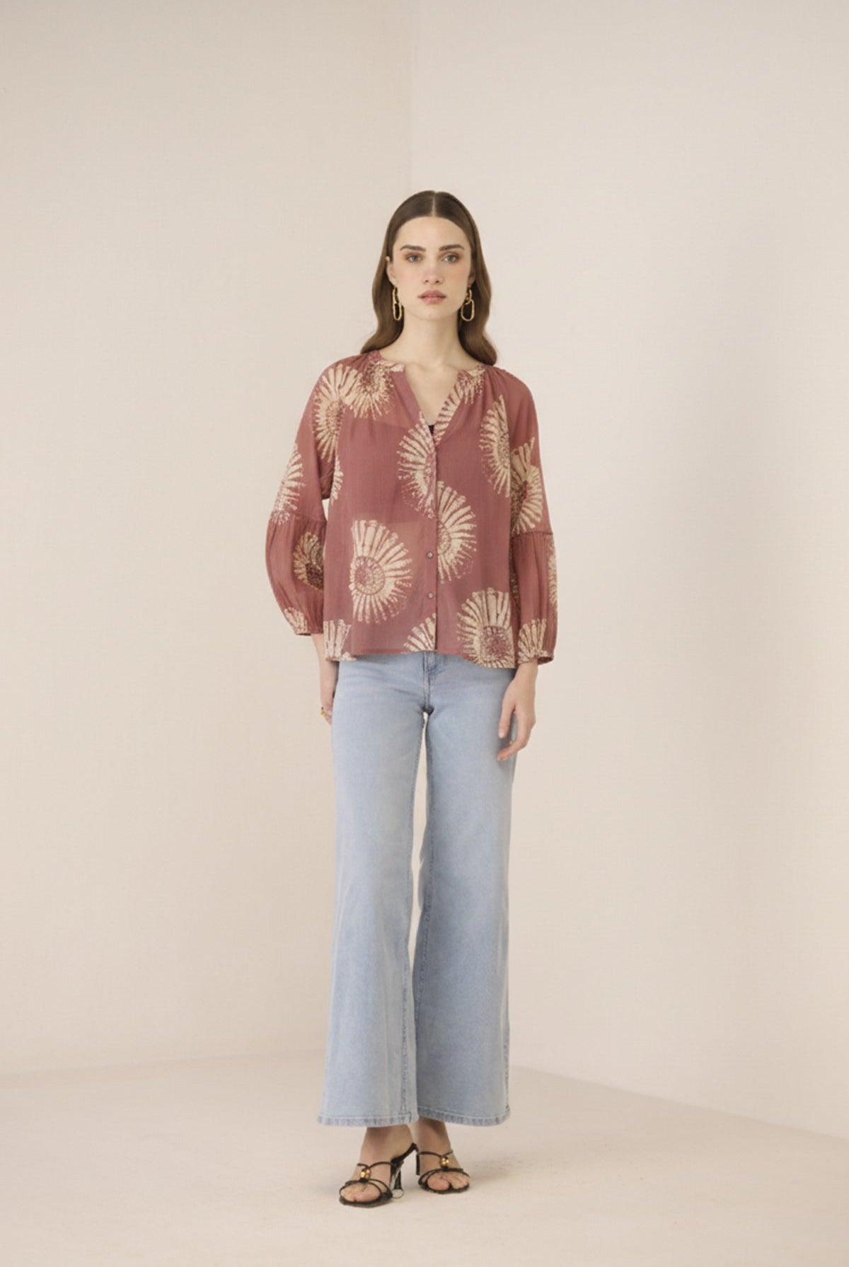 Woman wearing a patterned blouse and light blue pants on a beige background Calling June