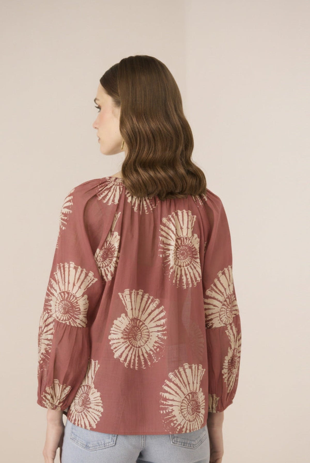 Woman wearing a rust-colored blouse with beige floral patterns on a plain background Calling June