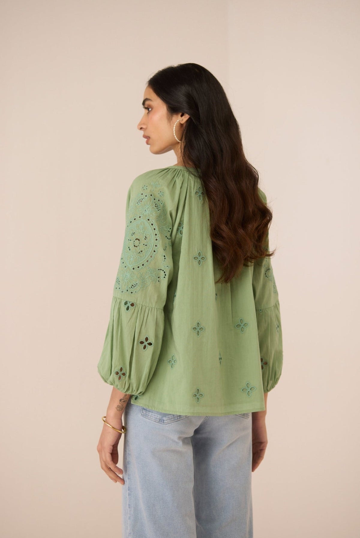 Woman wearing a green embroidered blouse with light blue jeans on a beige background Calling June