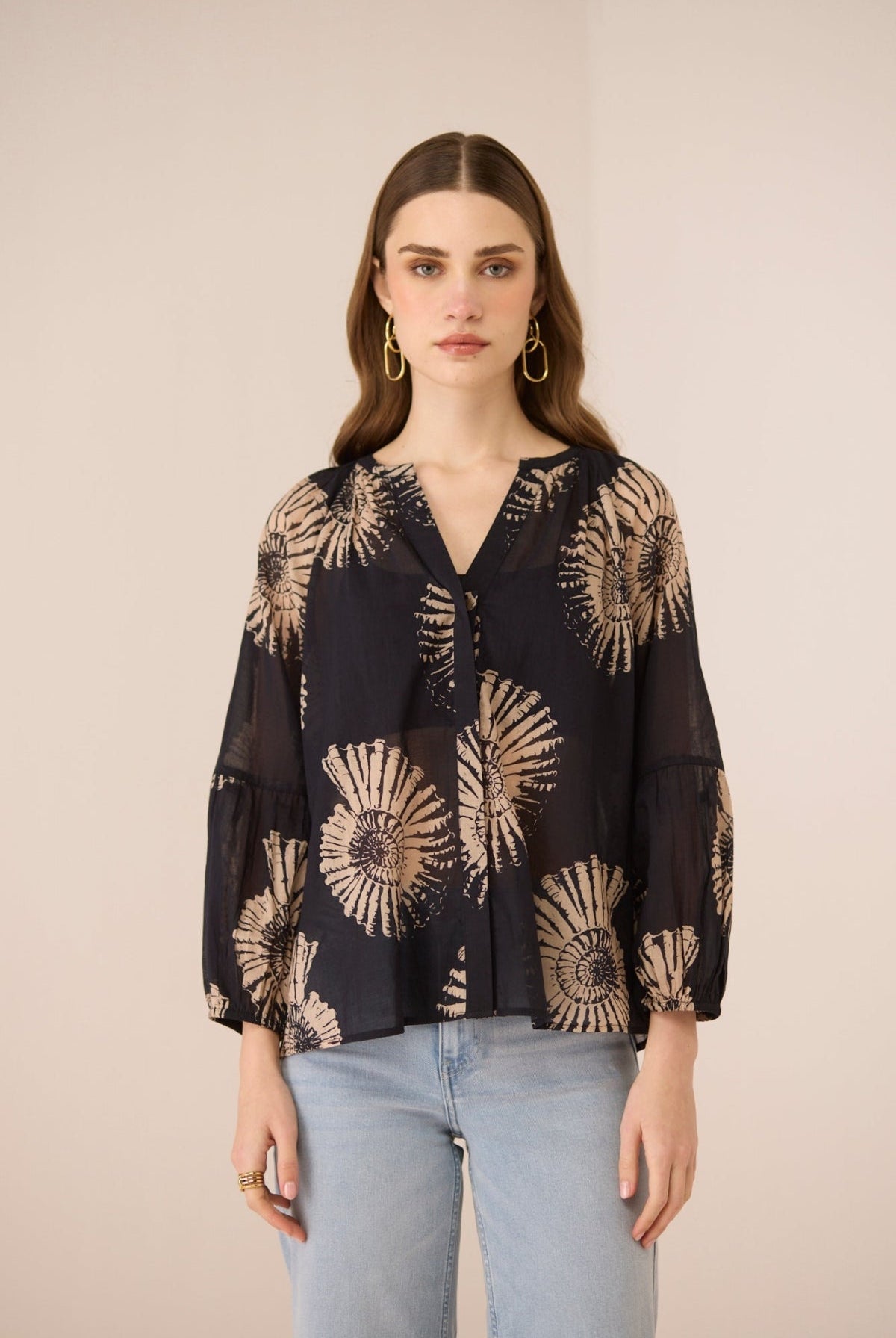 Woman wearing a black blouse with gold floral patterns on a beige background Calling June