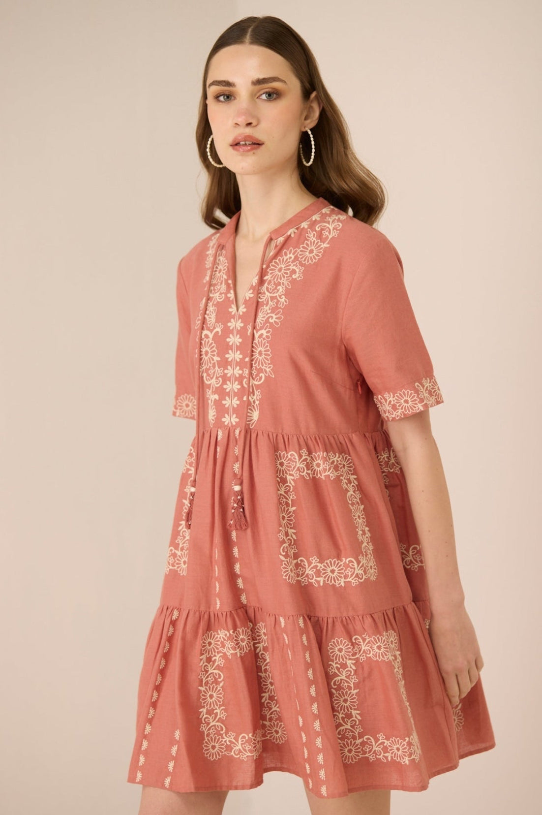 Woman wearing a pink embroidered dress against a beige background Calling June
