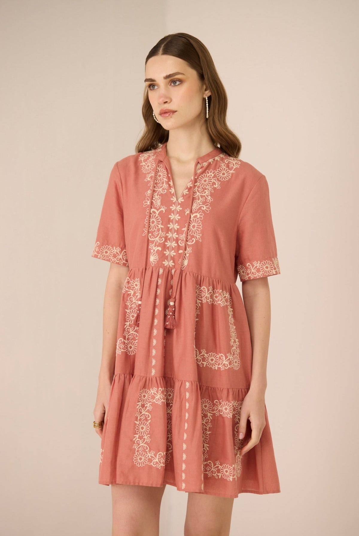 Woman wearing a pink dress with white embroidery on a beige background Calling June