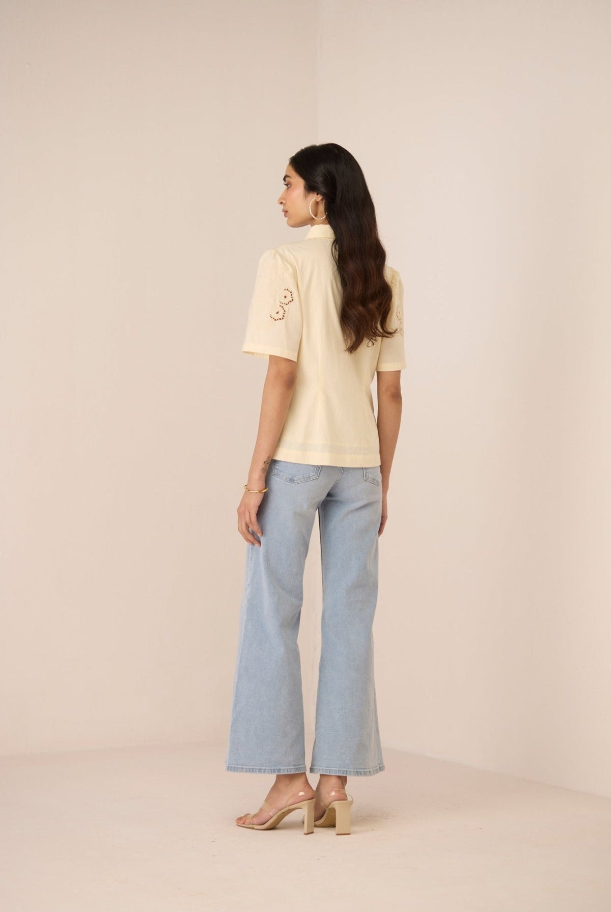 Woman wearing a cream top and light blue jeans on a beige background Calling June