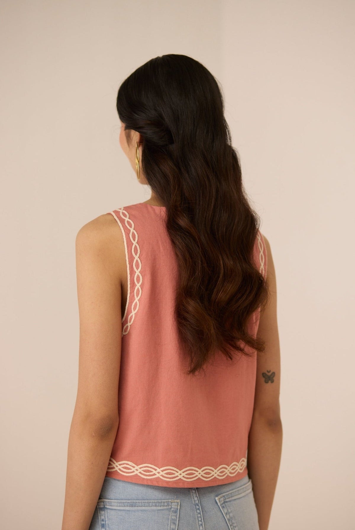 Woman wearing a pink sleeveless top with decorative back straps against a beige background Calling June