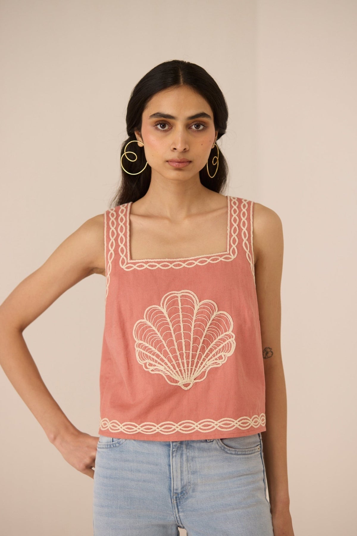 Woman wearing a pink tank top with shell design and lace details on a beige background Calling June