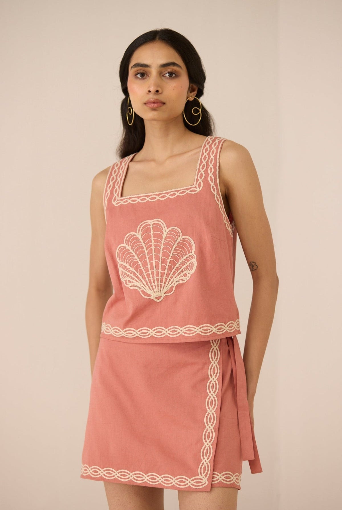 Woman wearing a pink dress with white shell design on a plain background Calling June