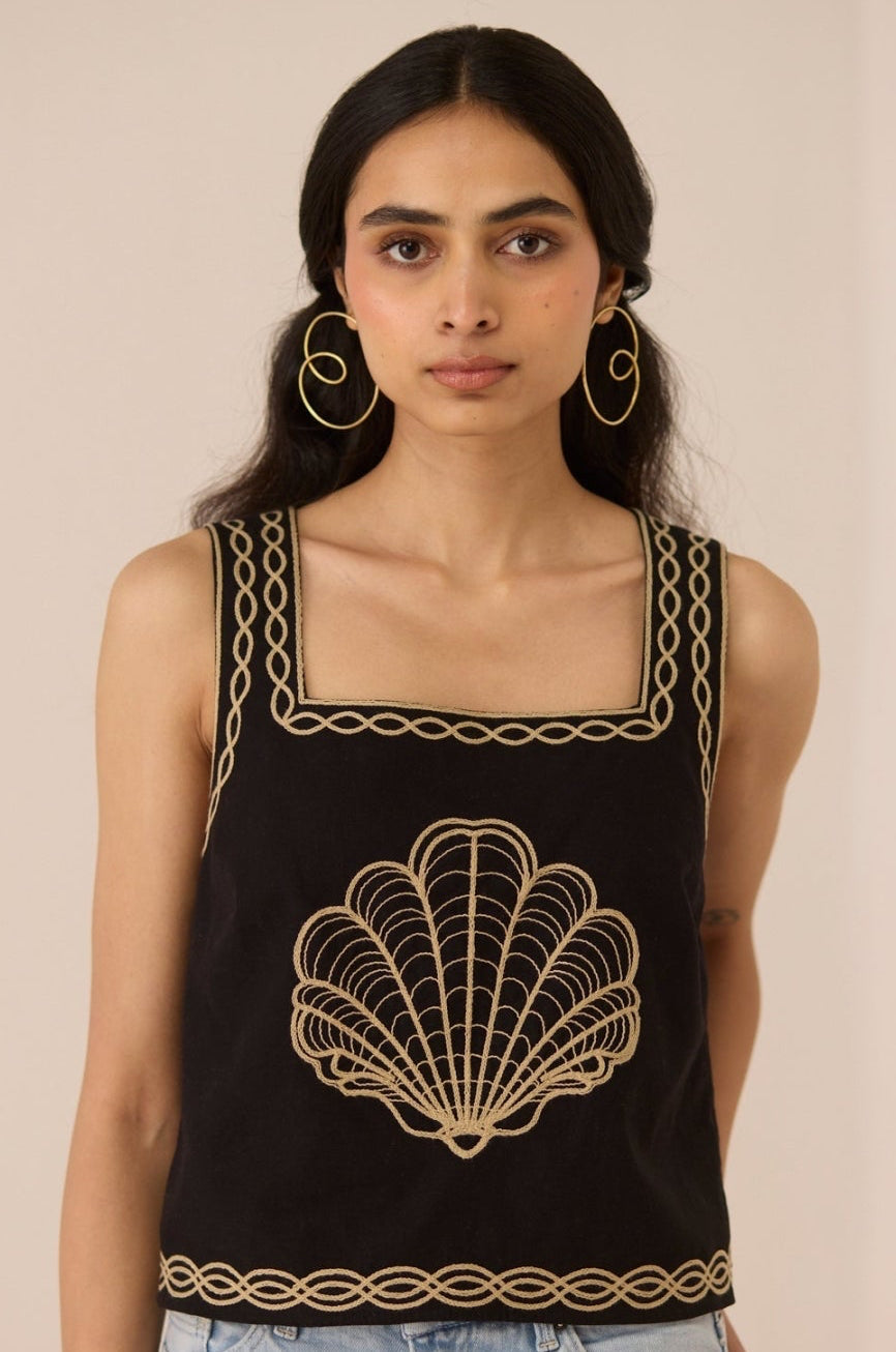 Woman wearing a black sleeveless top with gold embroidery against a beige background Calling June