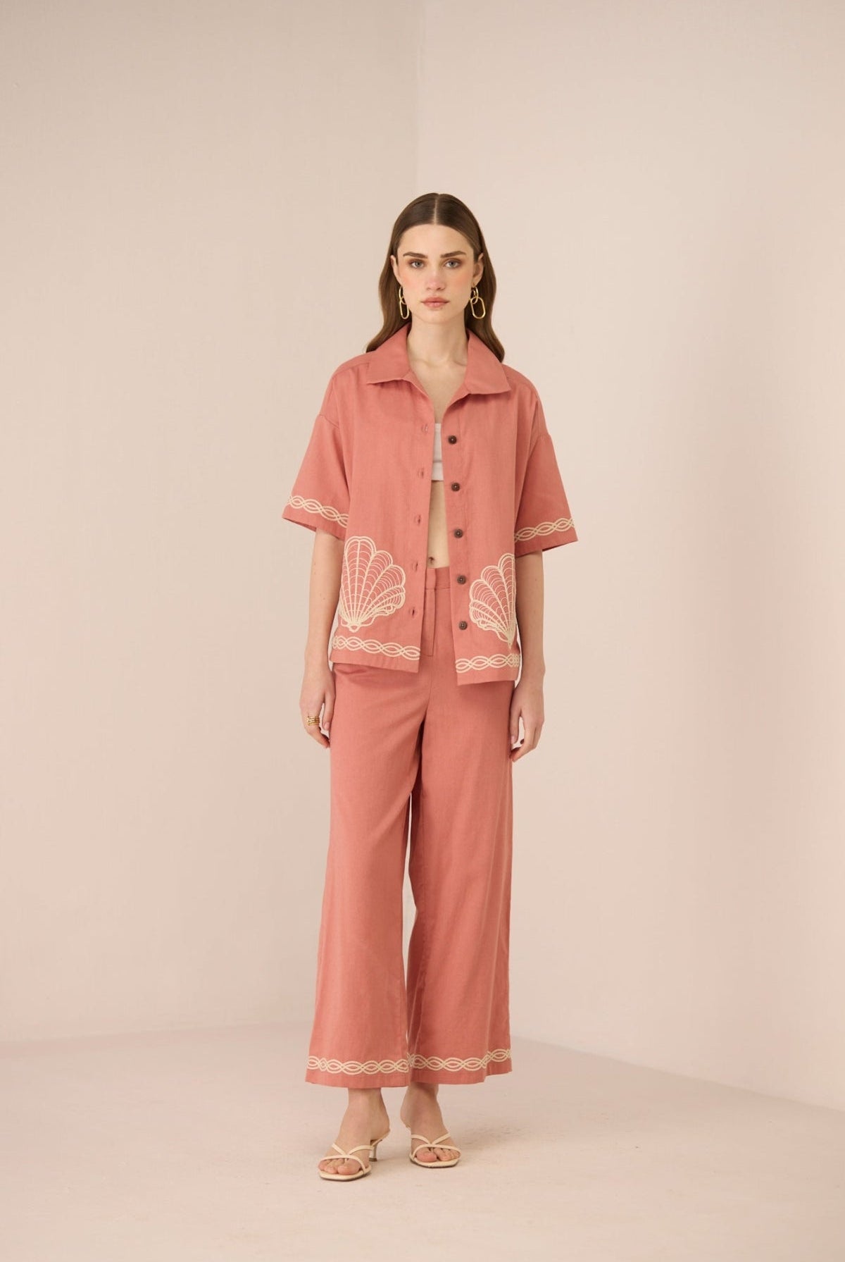 Woman wearing a pink outfit with shell patterns on a beige background Calling June