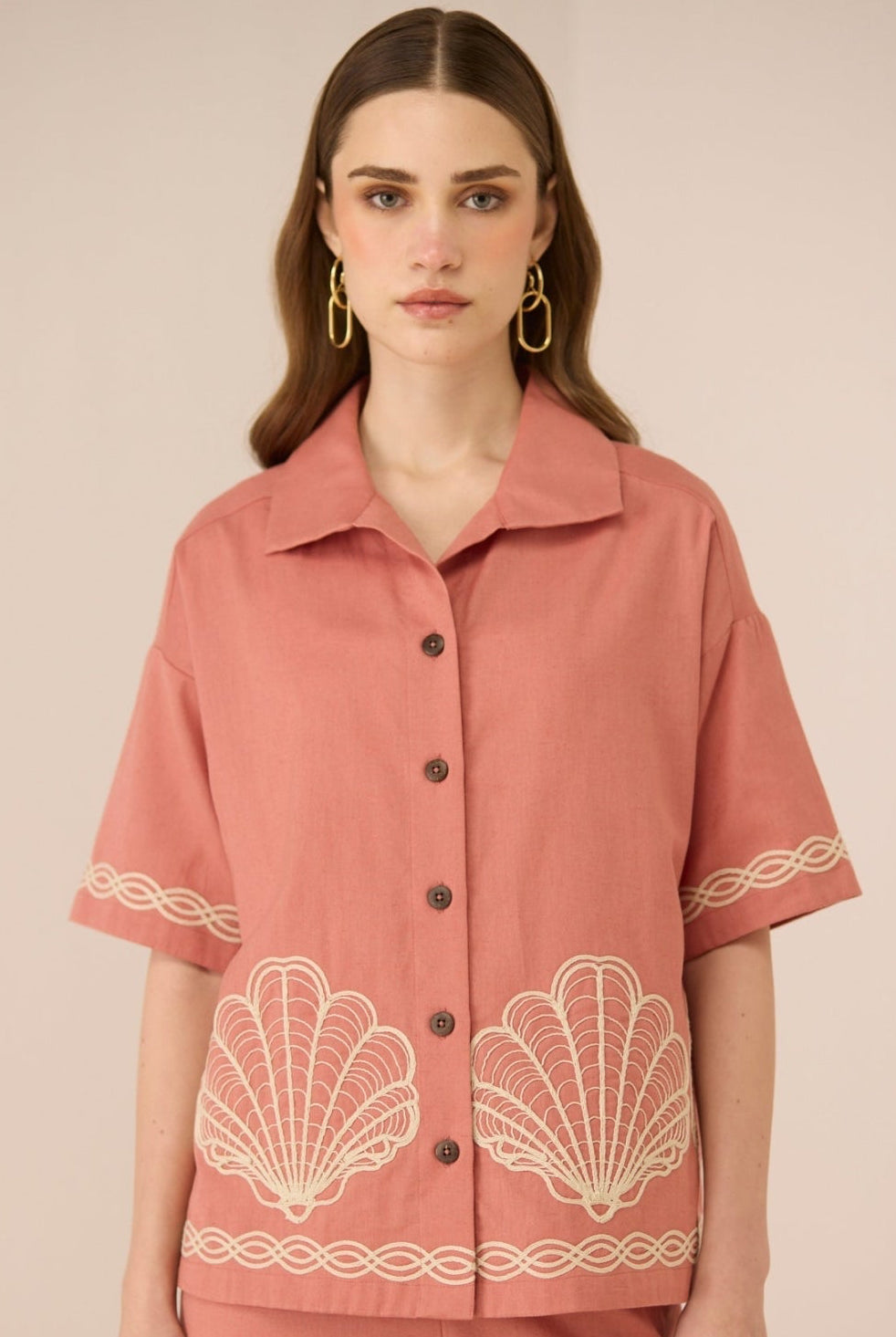 Woman wearing a pink blouse with shell patterns on a beige background Calling June