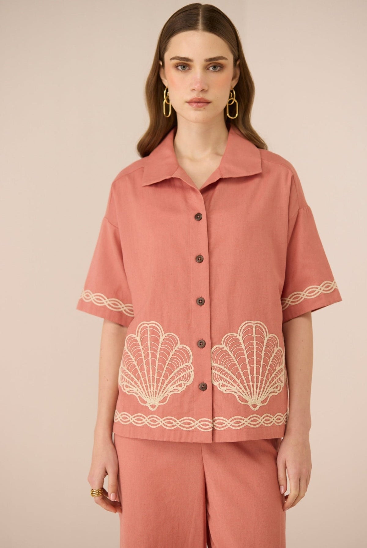 Woman wearing a pink blouse with shell patterns on a beige background Calling June