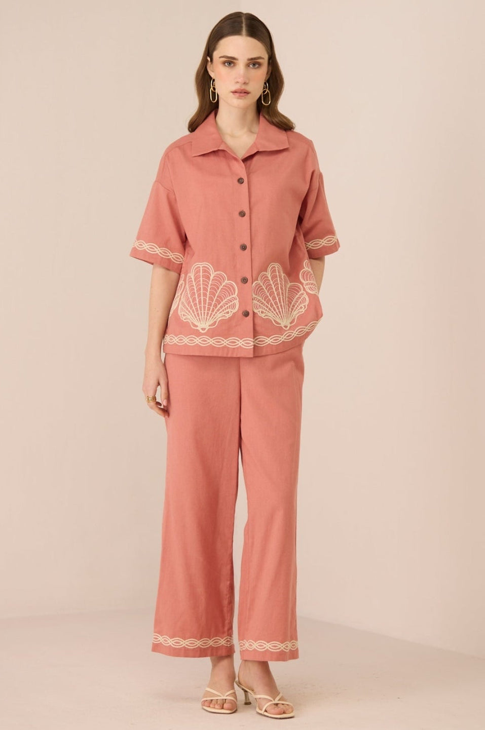 Woman wearing a pink outfit with shell patterns on a beige background Calling June
