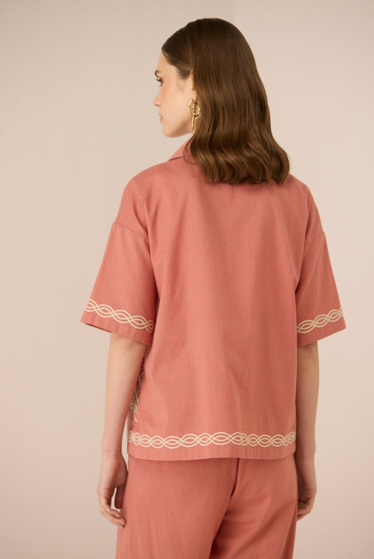 Person wearing a pink outfit with white embroidery on a beige background Calling June