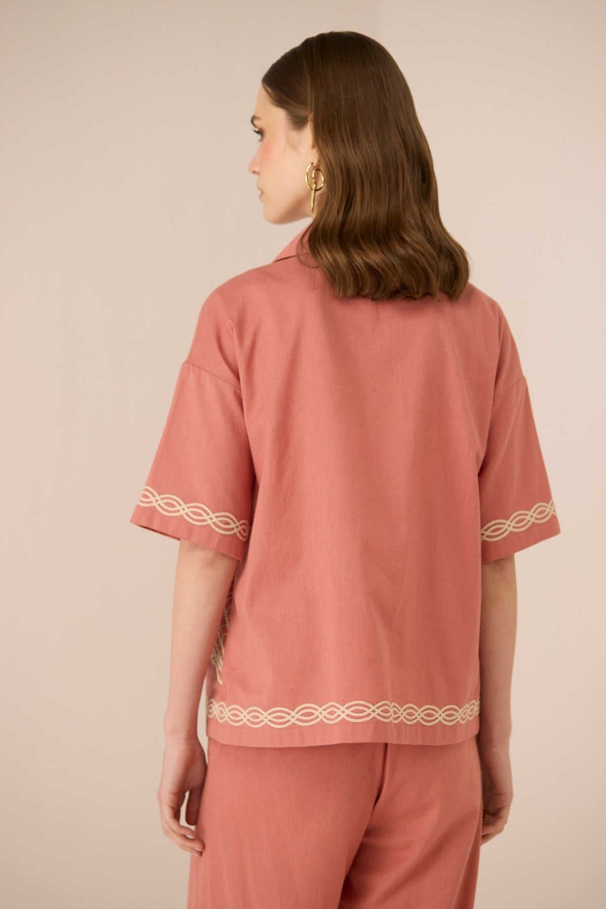 Person wearing a pink outfit with white embroidery on a beige background Calling June