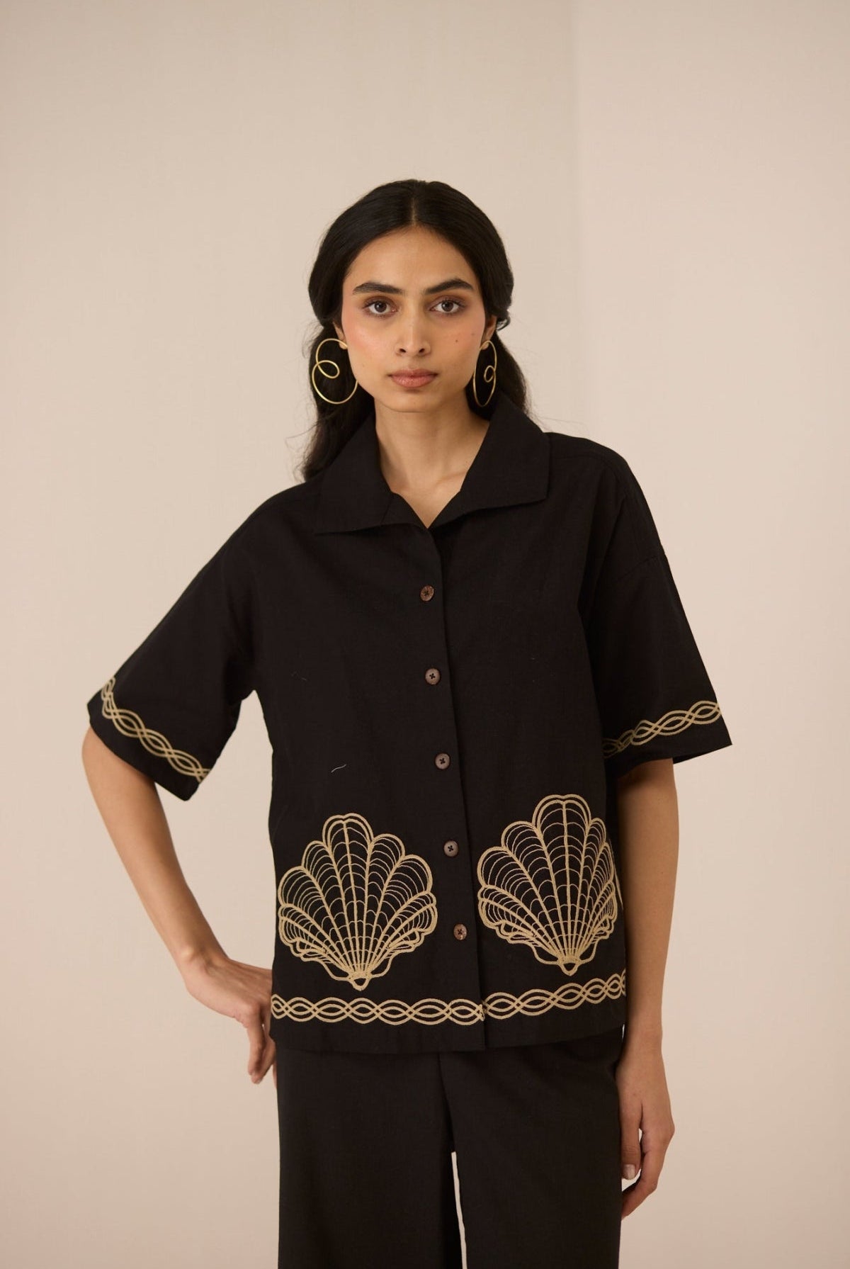 Woman wearing a black blouse with gold embroidery on a beige background Calling June