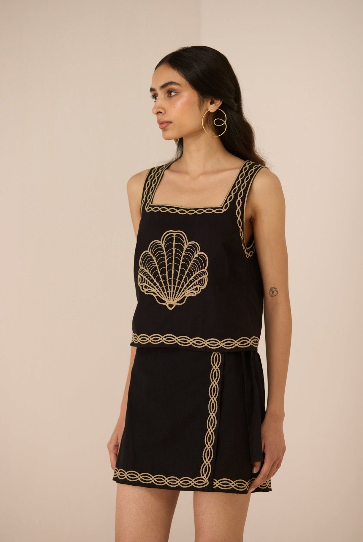 Woman wearing a black dress with gold embroidery against a beige background Calling June