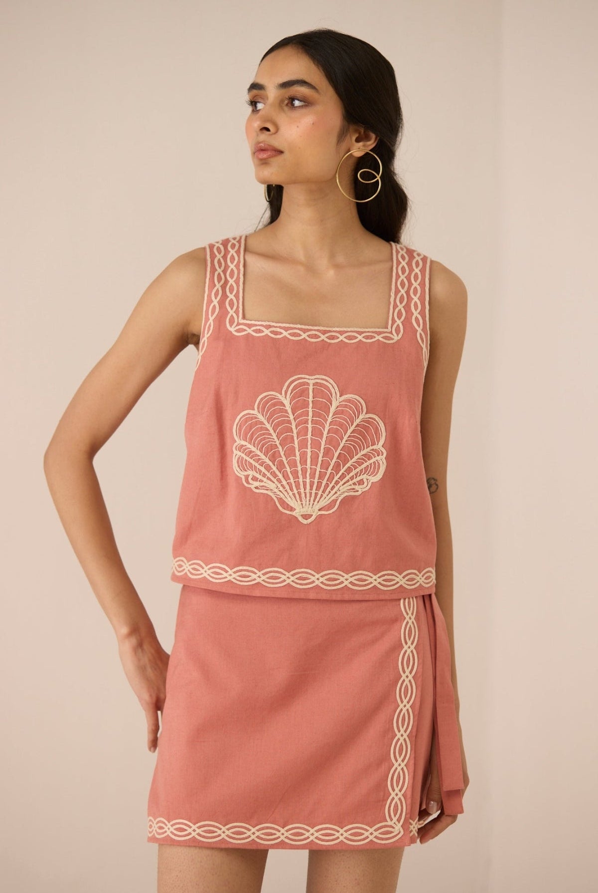 Woman wearing a pink dress with shell design on a beige background Calling June