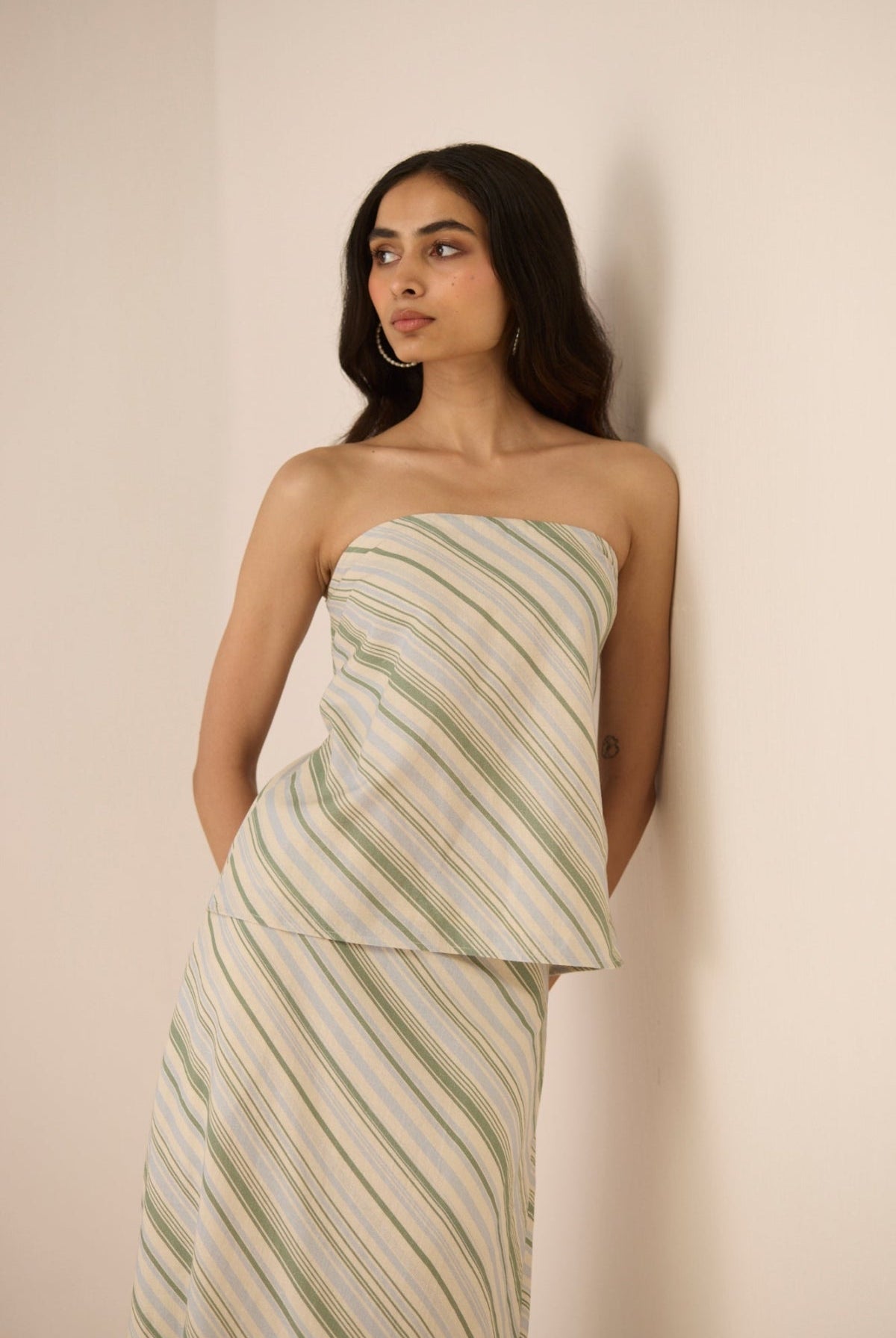 Woman wearing a strapless, green and white striped dress against a beige background Calling June