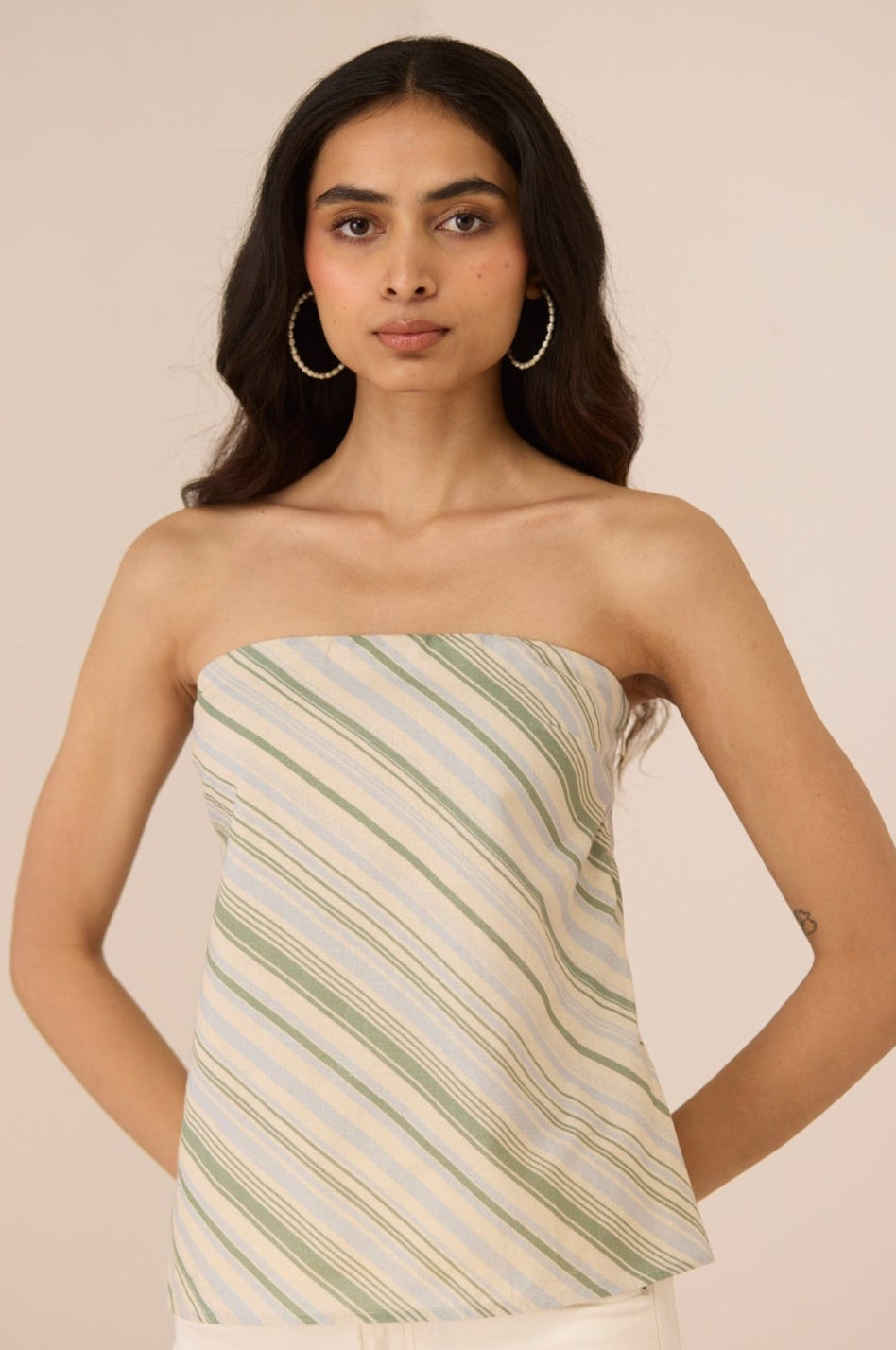 Woman wearing a strapless top with green and white stripes against a beige background Calling June