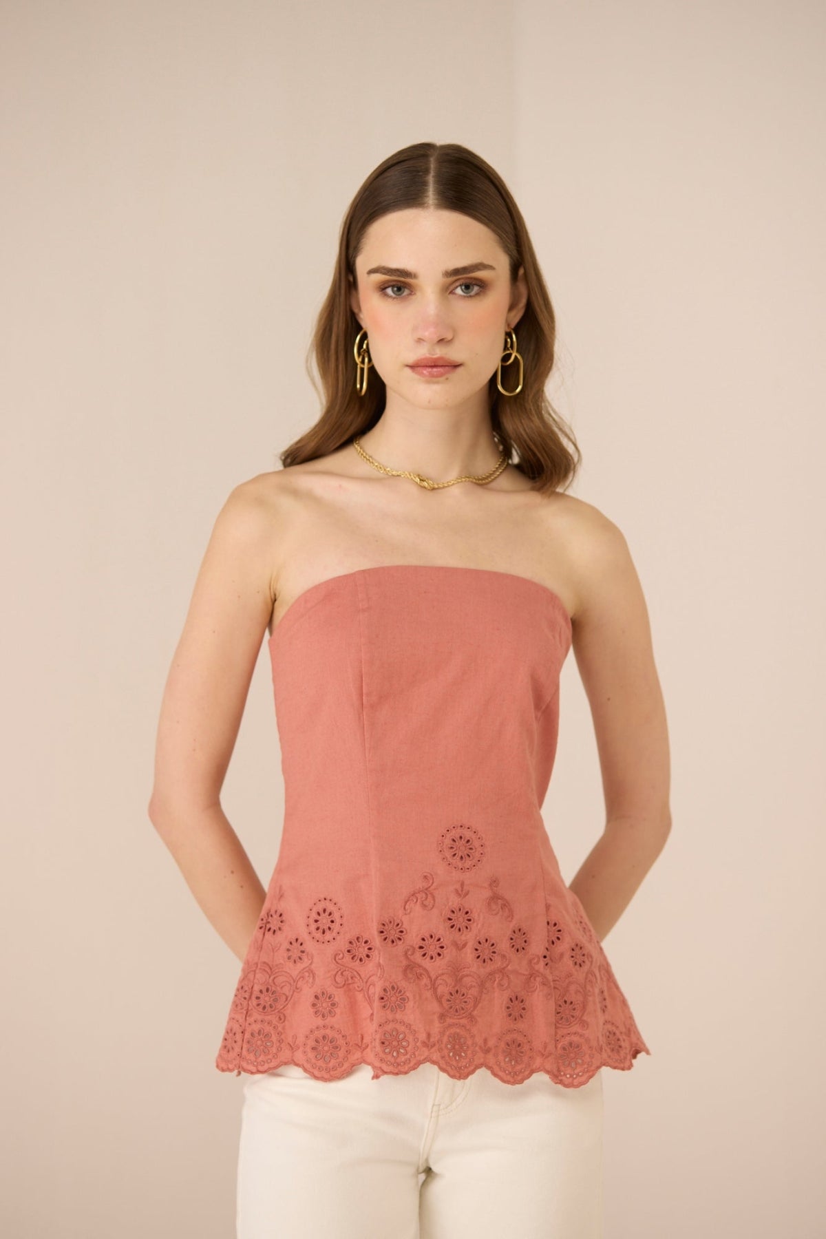 Woman wearing a pink strapless top with floral lace details on a beige background Calling June