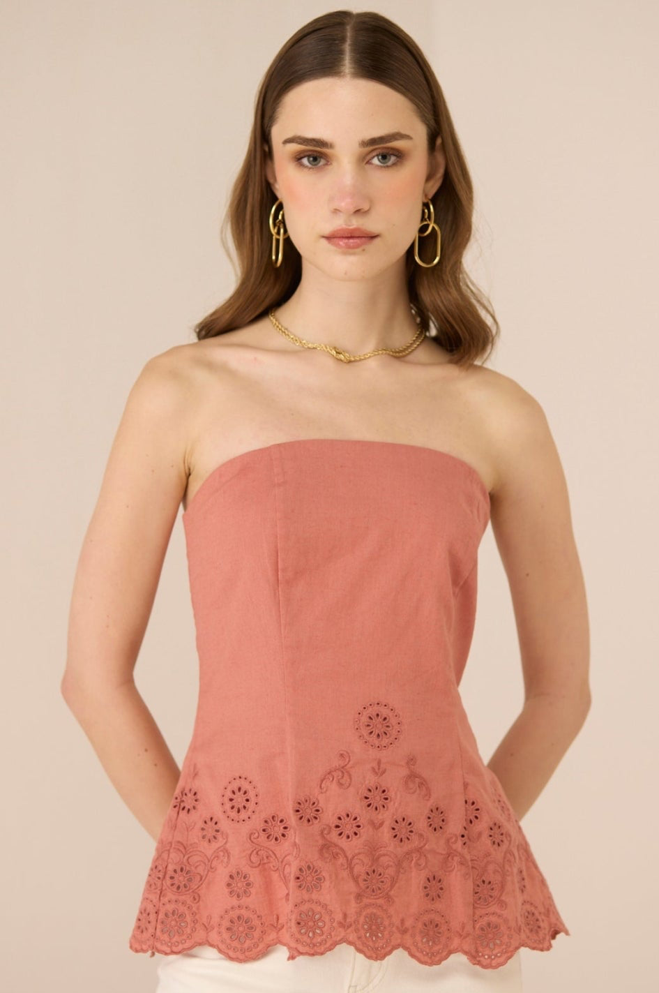 Woman wearing a pink strapless top with floral lace details on a beige background Calling June