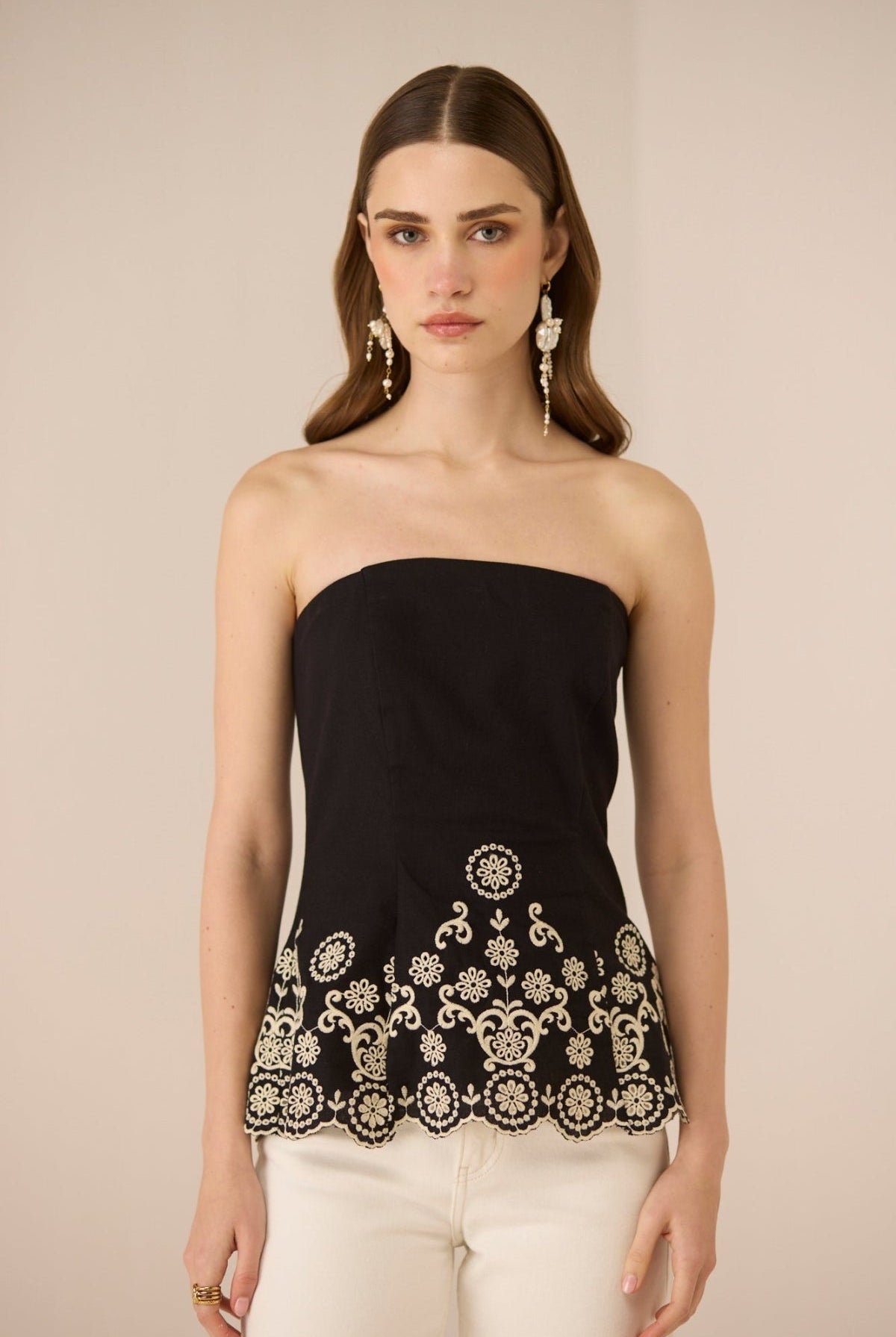 Woman wearing a black strapless top with white embroidery on a beige background Calling June