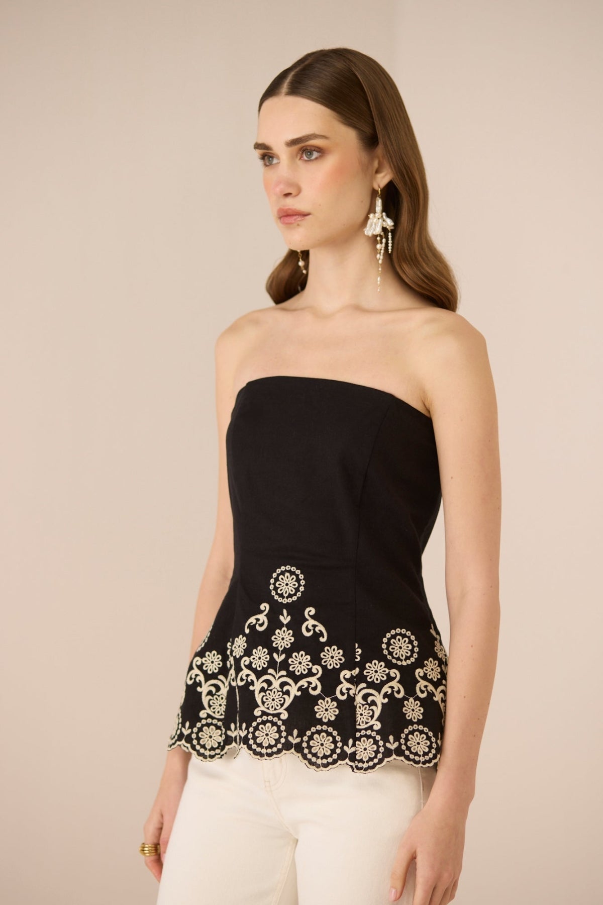 Woman wearing a black strapless top with white lace details on a beige background Calling June