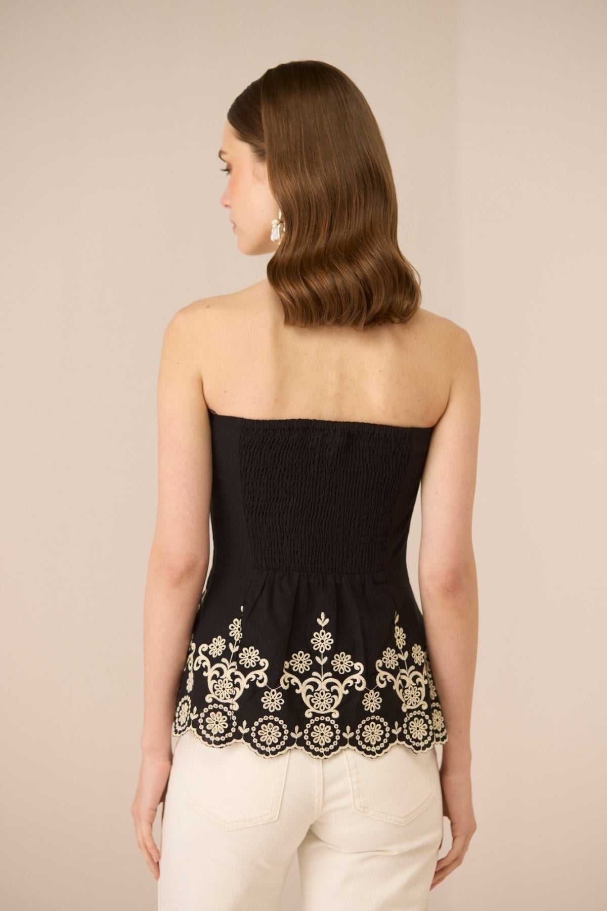 Woman wearing a black strapless top with white embroidery on a beige background Calling June