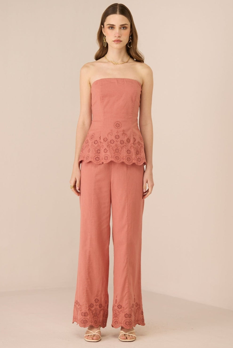 Woman wearing a pink strapless top and pants with lace details on a beige background Calling June