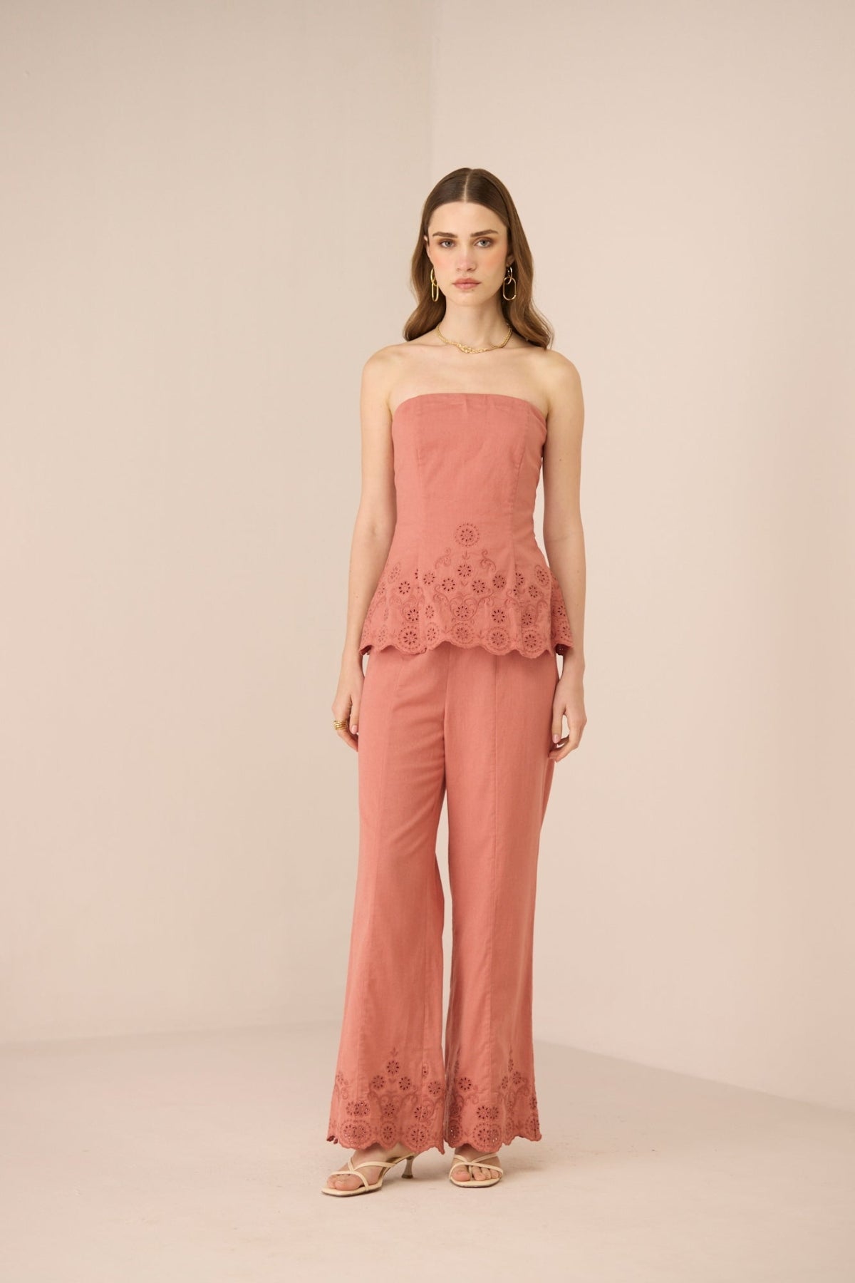 Woman wearing a pink strapless top and pants with lace details on a beige background Calling June