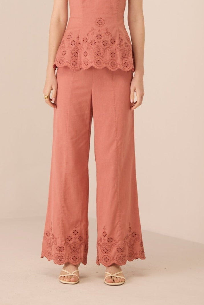 Woman wearing a coral strapless top and wide-leg pants with lace details on a beige background Calling June